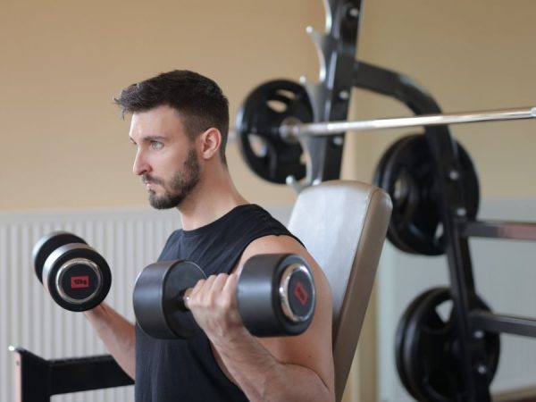 Focused man lifting dumbbells for bicep curls in gym, emphasizing strength and fitness.